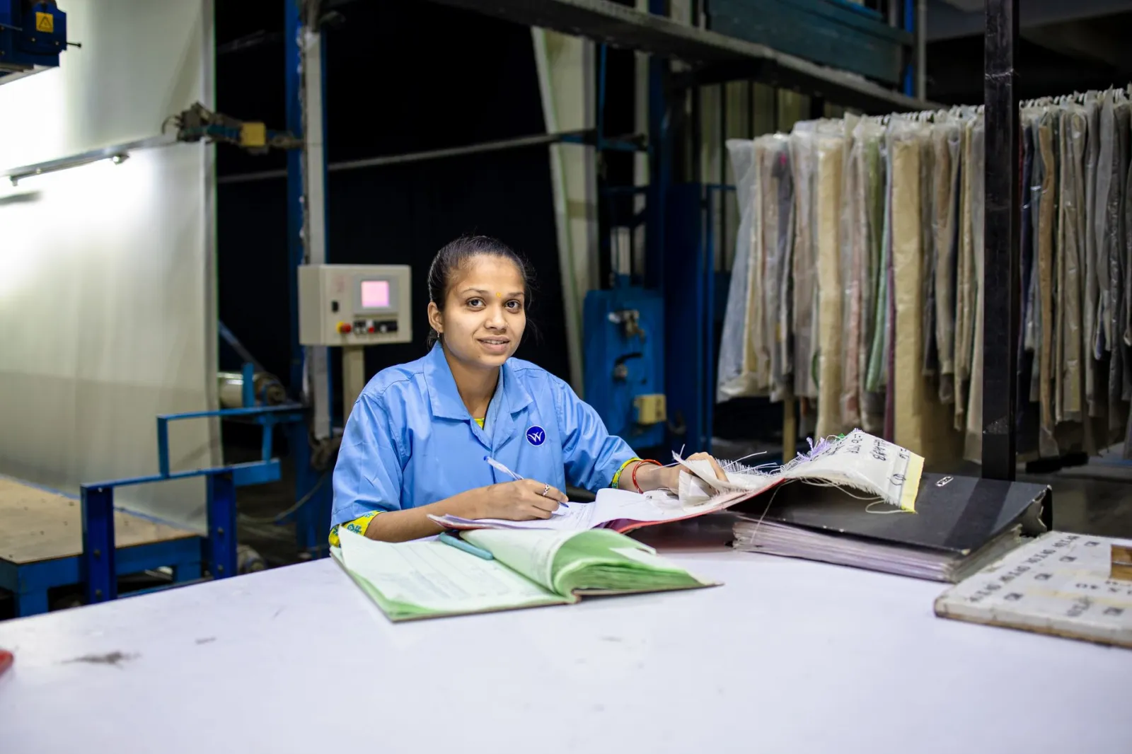 Female textile worker in factory reviewing documents at a desk.