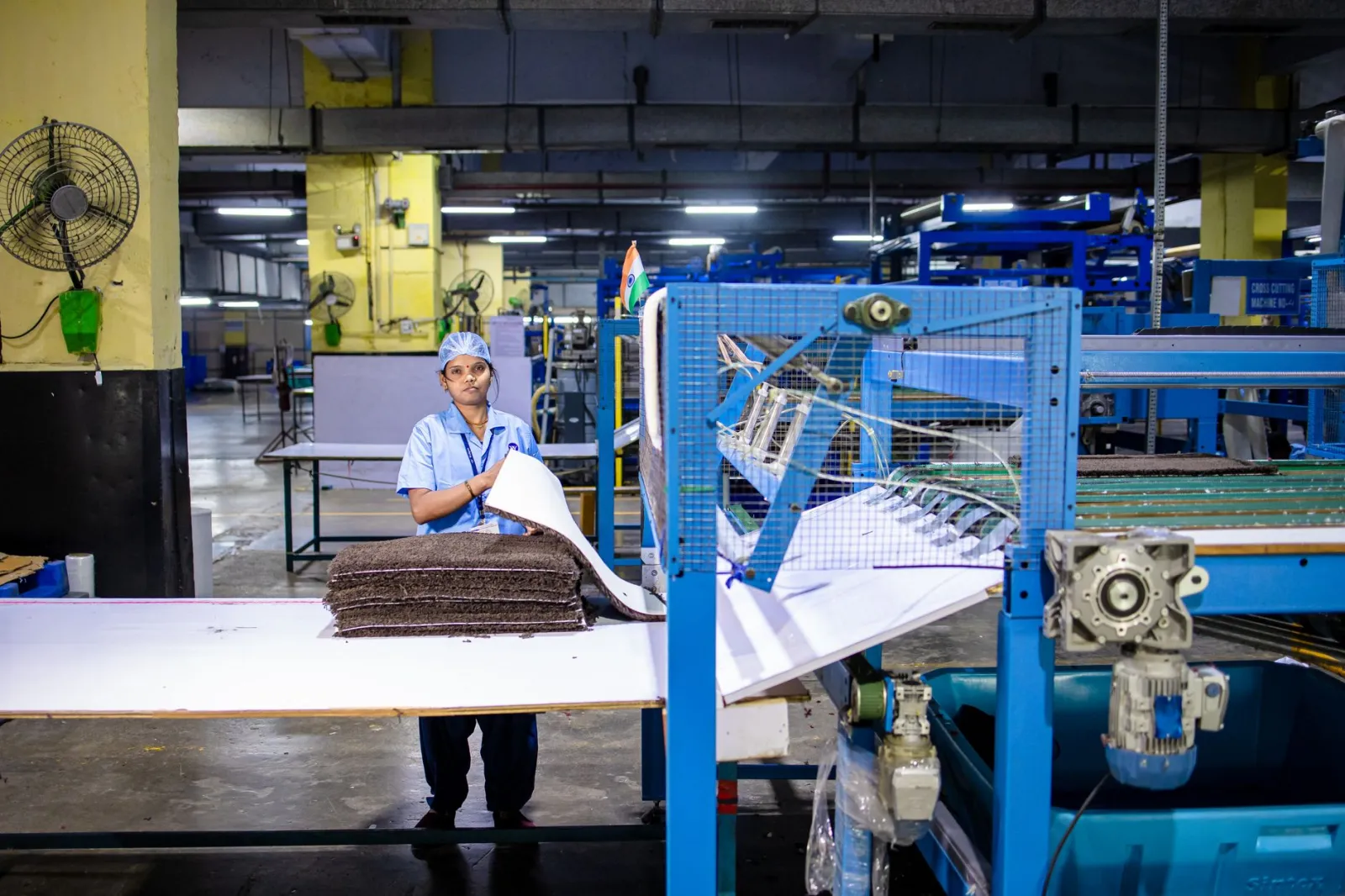 Woman in uniform working in a textile factory, handling materials at a processing machine.